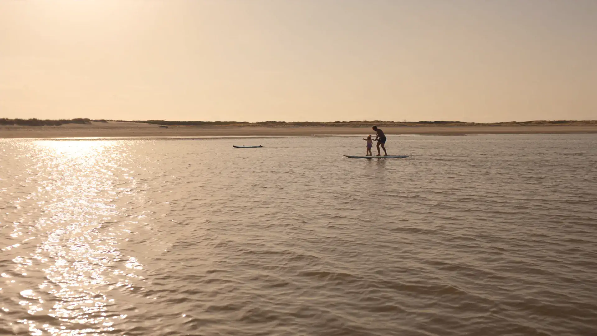 Vader en kind suppen op een ondiep Nederlands strand in de zomer